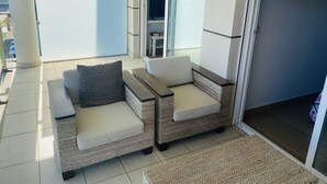 Un balcón con mobiliario de mimbre, una puerta de cristal que da a una habitación y un suelo de baldosas.