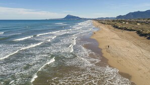 Una playa con olas, una persona caminando y montañas al fondo.