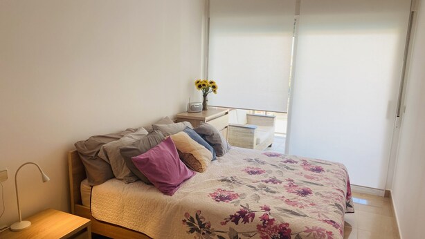 Un dormitorio con cama, mesita de noche, lámpara y vistas al exterior.