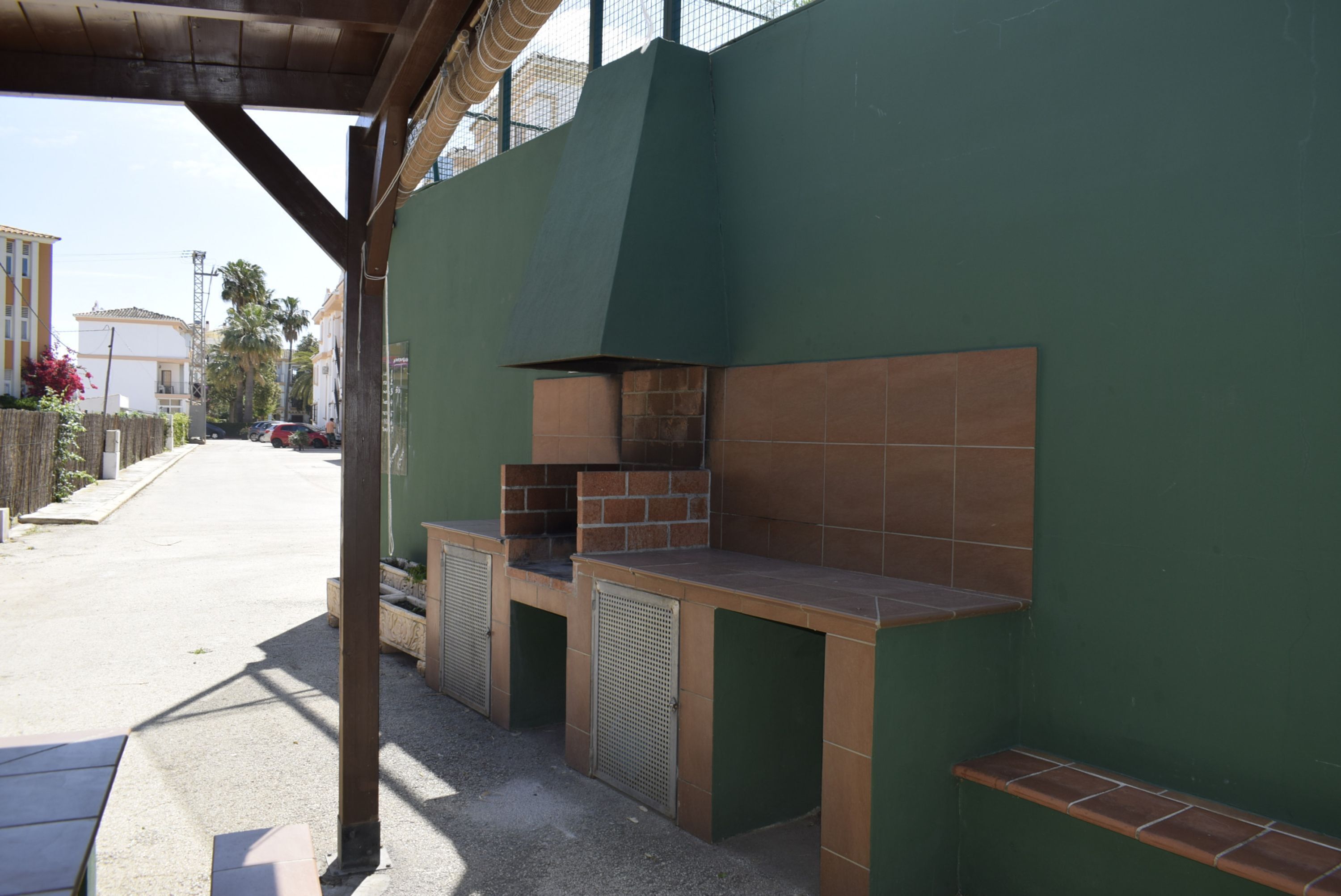An outdoor kitchen area with a green wall and a brick oven, adjacent to a building with a tiled roof.