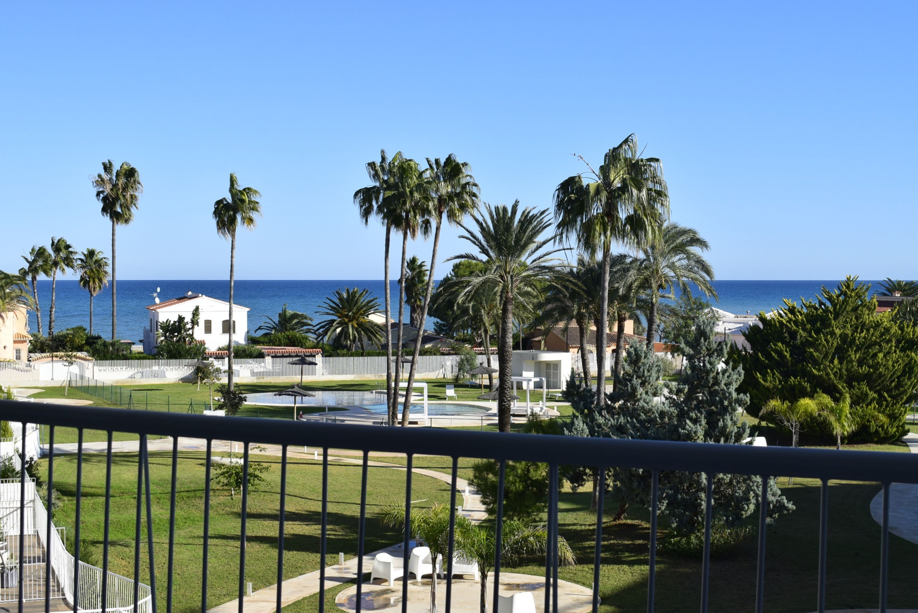 Une vue d’un complexe hôtelier avec une piscine, des palmiers et un ciel bleu azur.