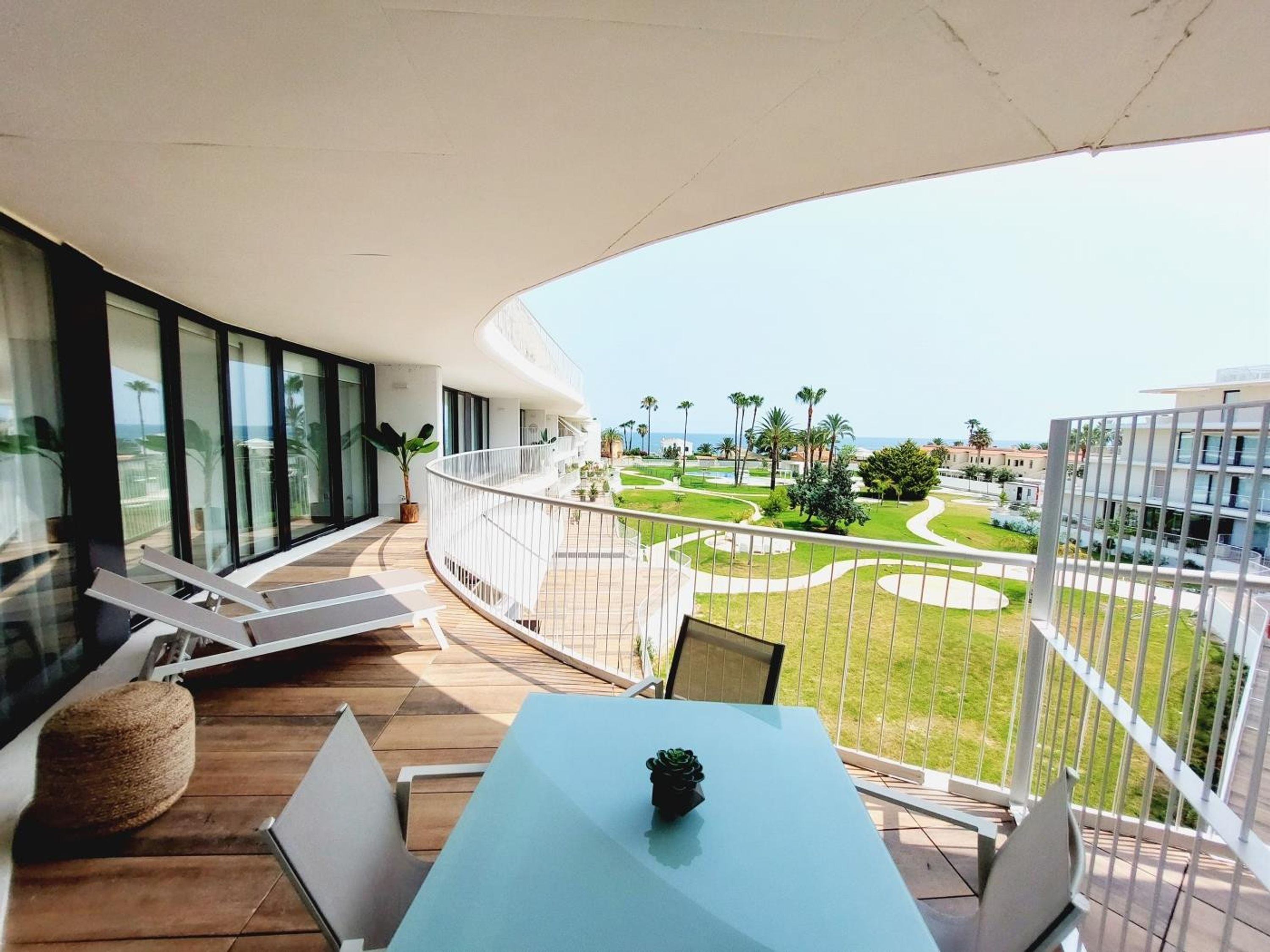 A balcony with a table and chairs, overlooking a landscaped garden and buildings.