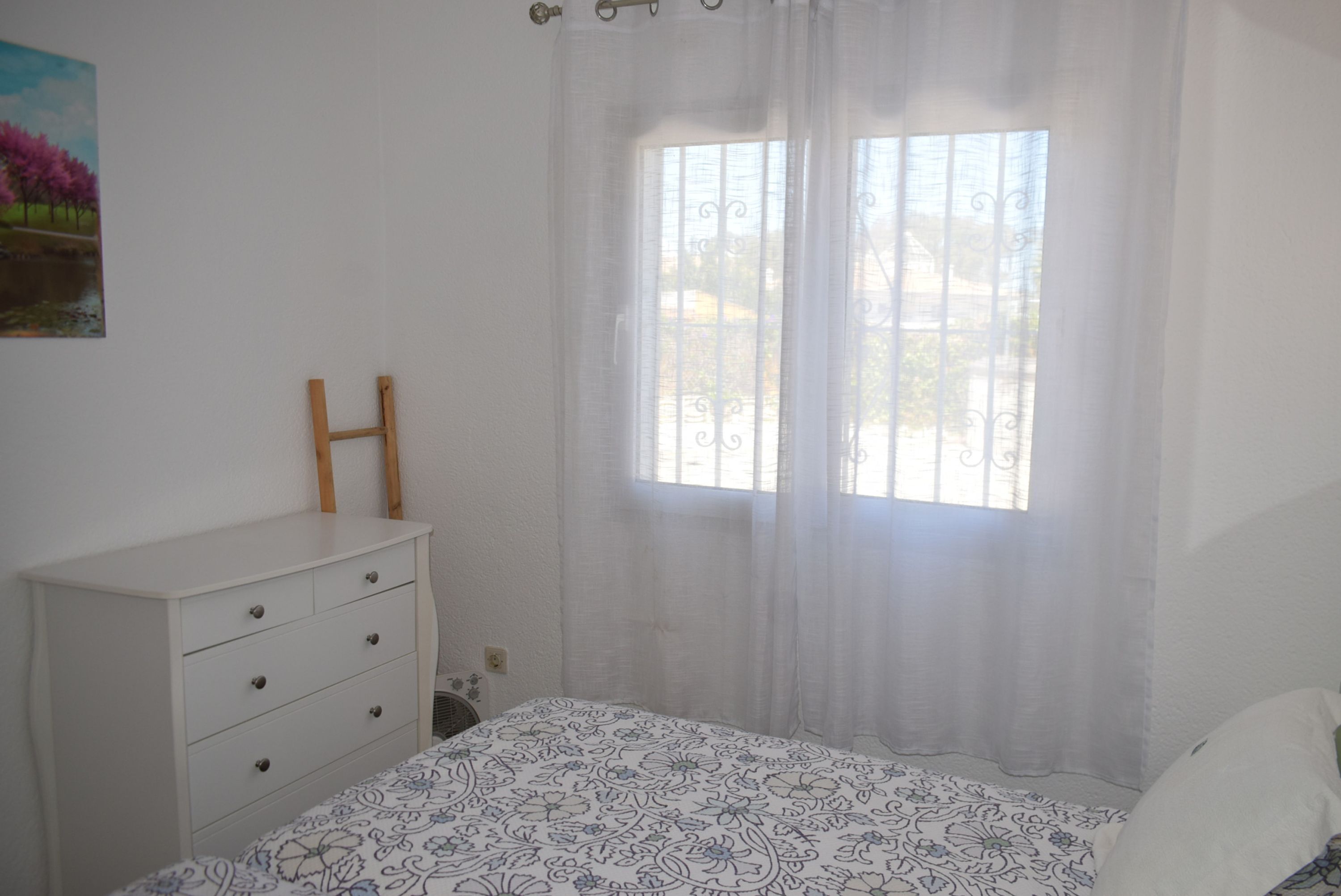 A bedroom with a bed, a dresser, a window with curtains, and a painting on the wall.