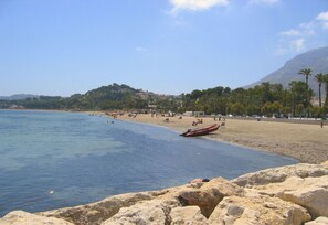 Una playa con agua azul cristalina, costa rocosa y una montaña distante.