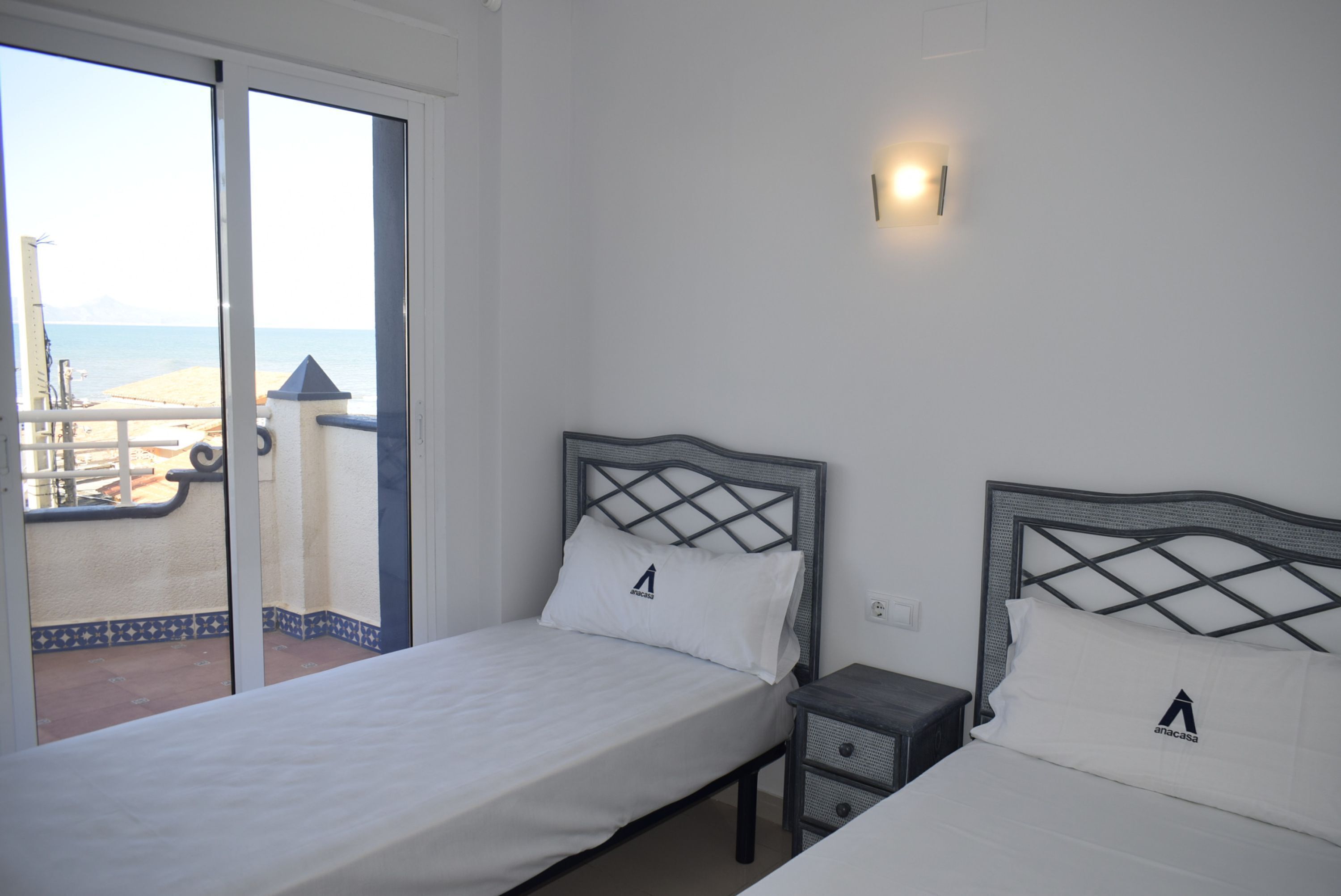 Ein Hotelzimmer mit Bett, Nachttisch und Blick auf den Strand durch eine Schiebetür.