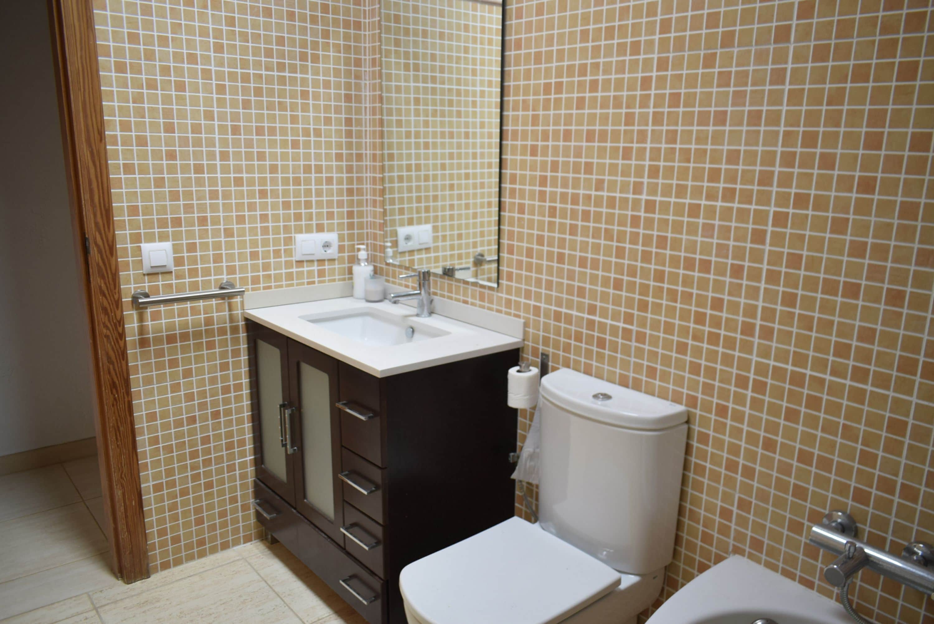 A bathroom with a tiled wall, a sink, a toilet, and a cabinet.