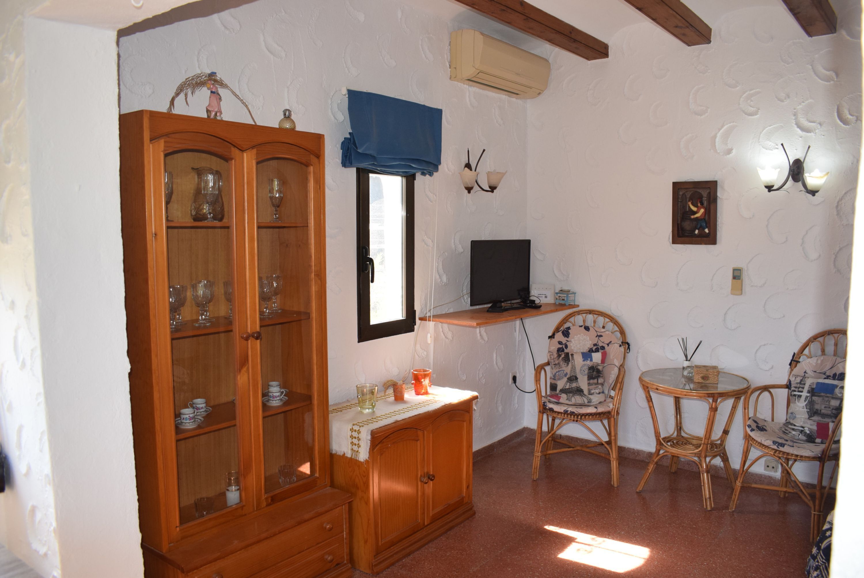 A room with a wooden cabinet, a television on a stand, wicker chairs, and a small table.