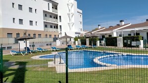 Una piscina circondata da una recinzione, con lettini e un edificio sullo sfondo.