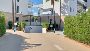 Ingresso moderno di un edificio con viale privato recintato, circondato da vegetazione e palme.
