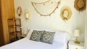 Una camera da letto con un letto, due cuscini con scritte, una mensola in legno, un comodino con una lampada e diversi cappelli appesi al muro.