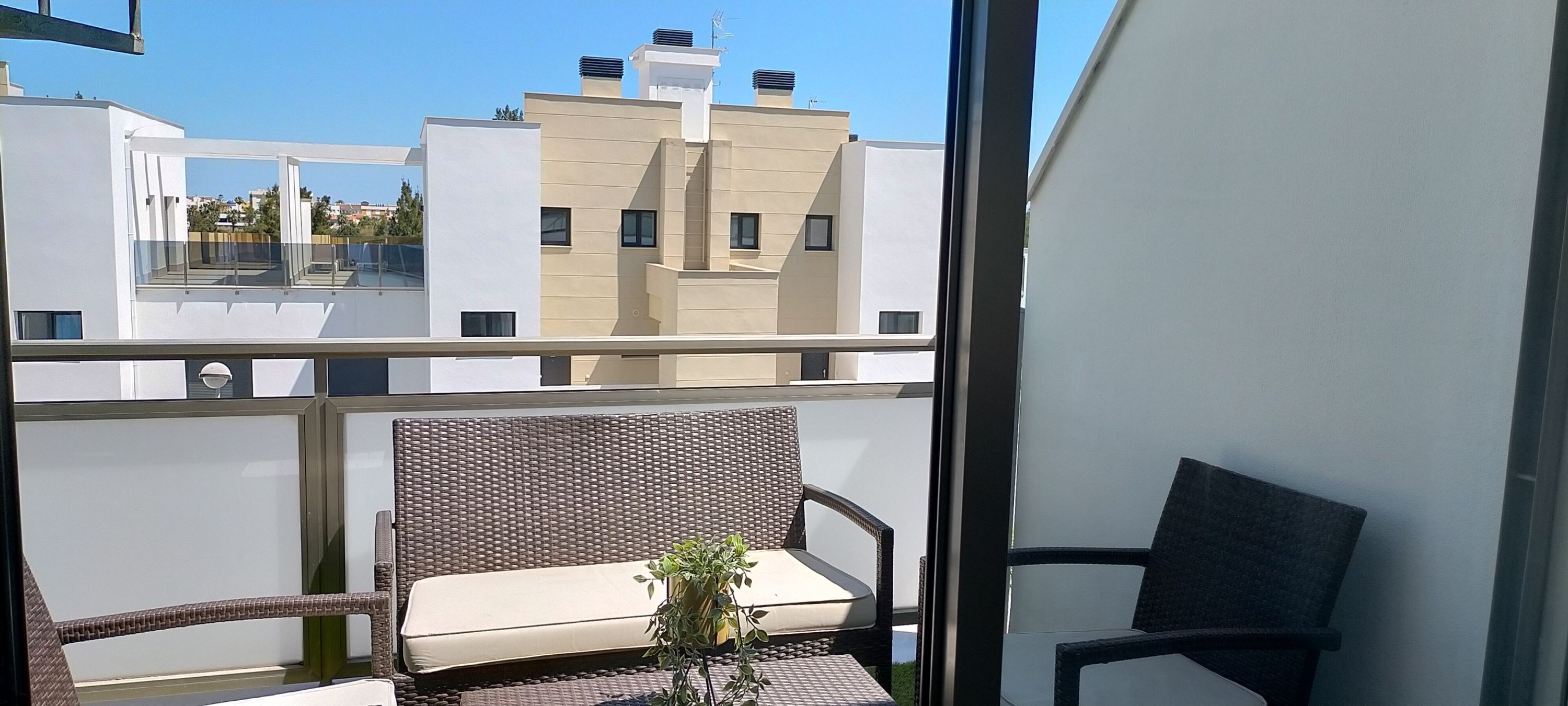 A balcony with wicker furniture, a cushioned bench, and a potted plant.