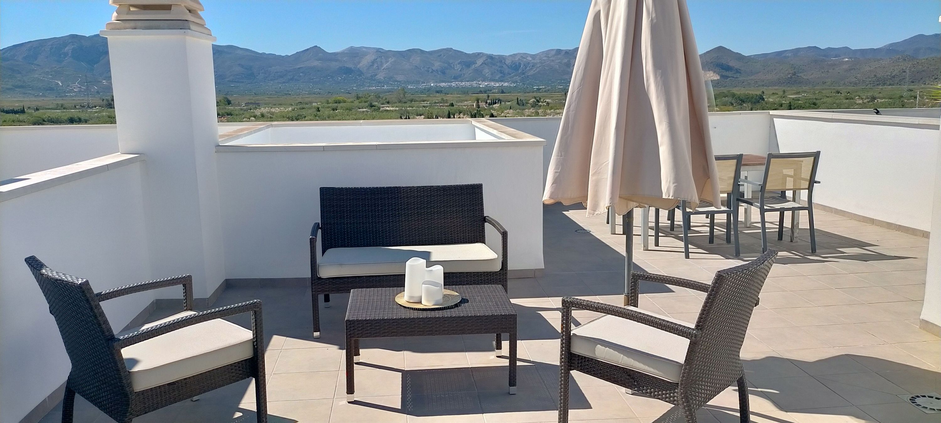 A rooftop terrace with wicker furniture, a table with candles, and a view of mountains.