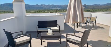 A rooftop terrace with wicker furniture, a table with candles, and a view of mountains.