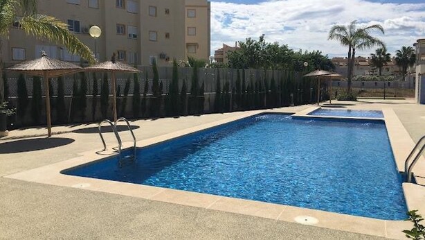 A rectangular swimming pool with two diving boards, surrounded by a low fence, palm trees, and a building in the background. - Ap625 in Oliva With 2 Bedrooms and 2 Bathrooms (Oliva)