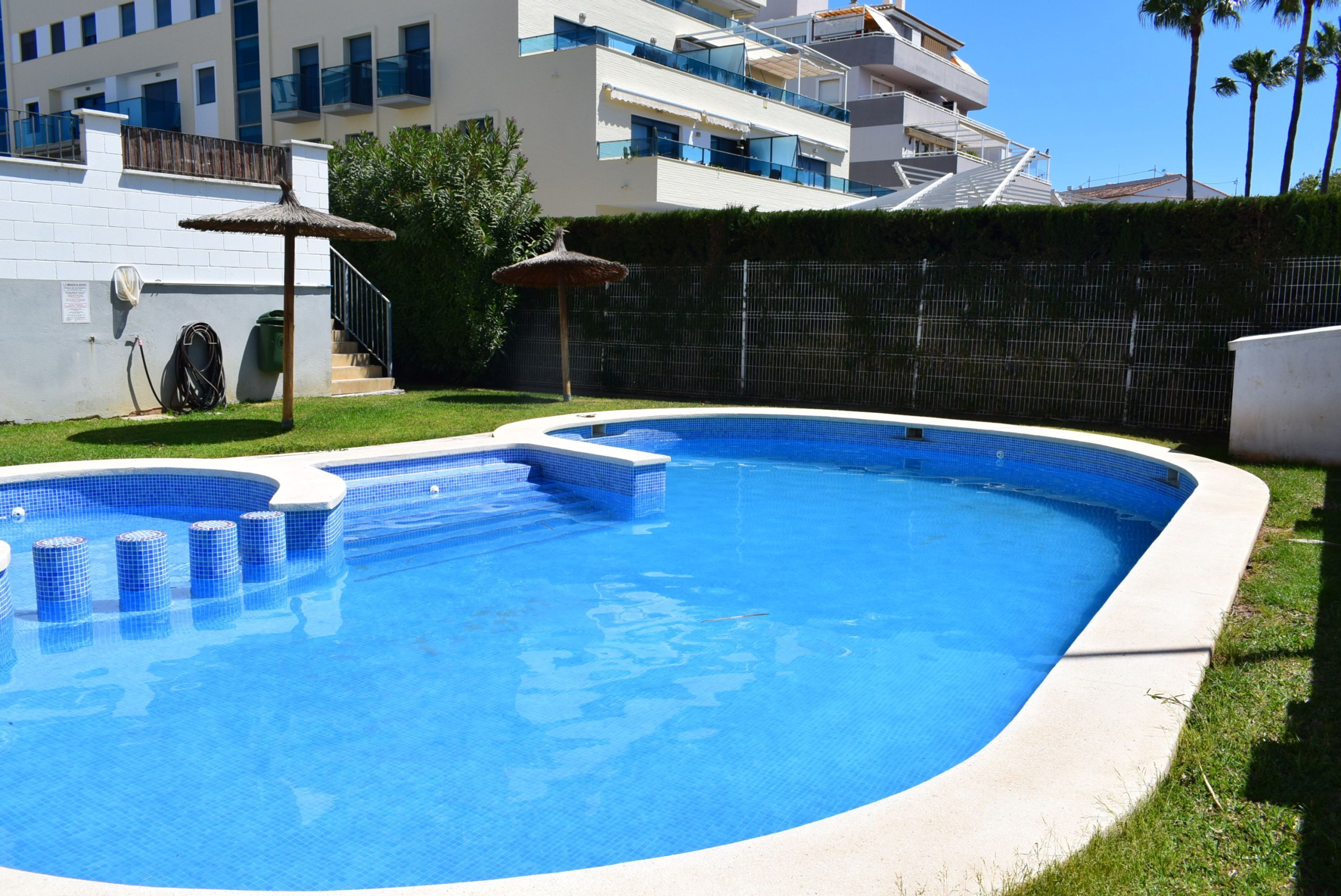 A swimming pool with a blue tiled interior, surrounded by a white wall and a grassy area.
