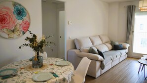 Ein Wohnzimmer mit einer Couch, einem Esstisch gedeckt mit Tellern und Gläsern sowie einem großen floralen Gemälde an der Wand.