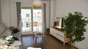 Ein modernes Wohnzimmer mit einer Couch, einem Fernseher, einem Esstisch und einer großen Pflanze.