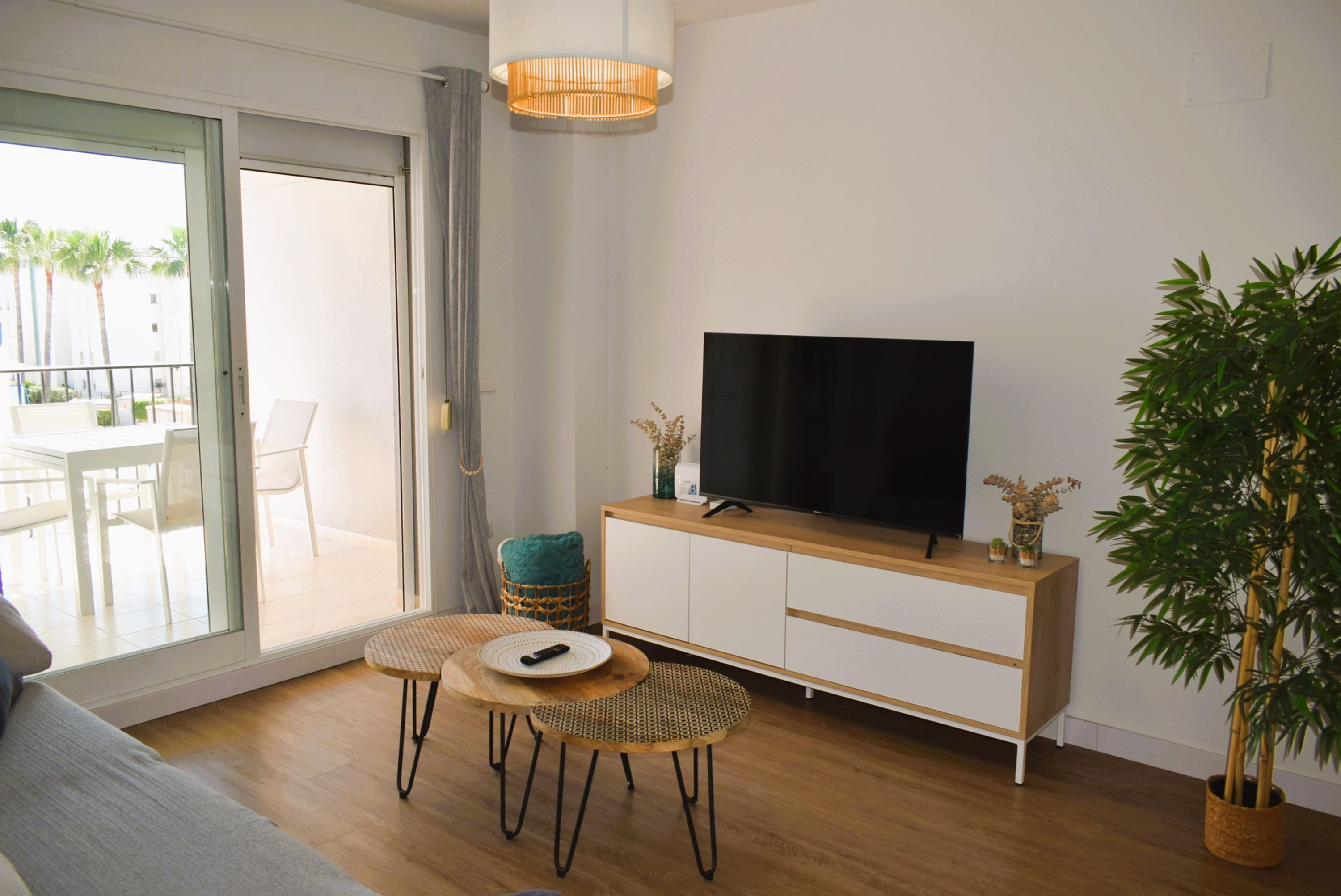 Una sala de estar moderna con un ventanal corredero que da a un espacio exterior, un televisor de pantalla plana sobre un mueble de madera y una planta grande en maceta.