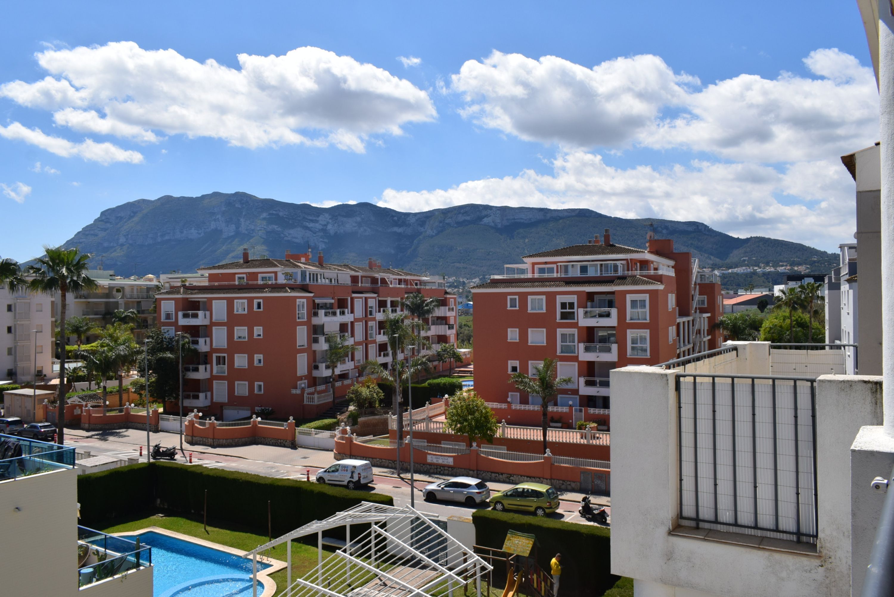 A residential area with apartment buildings, a swimming pool, and a mountain in the background.