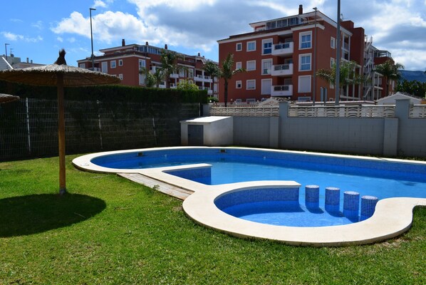 A swimming pool with a curved edge, surrounded by a well-maintained lawn and a fence. - Ap2238 in Denia With 2 Bedrooms and 2 Bathrooms (Denia)