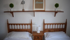 Ein Schlafzimmer mit zwei hölzernen Betten, einem Nachttisch mit Lampe sowie einem Regal mit zwei Blumentöpfen und einem gerahmten Bild.