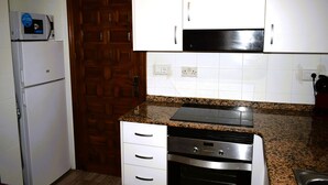 Eine Küche mit weißen Schränken, einer Granitarbeitsplatte, einem eingebauten Backofen und einer Mikrowelle auf einem weißen Kühlschrank.