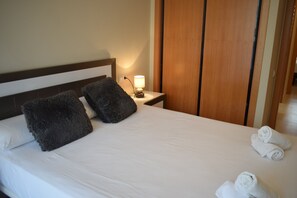 A neatly made bed with white linens and two dark gray pillows, a bedside lamp, and two rolled white towels on the side. - Ap2213 in Denia With 2 Bedrooms and 2 Bathrooms (Denia)
