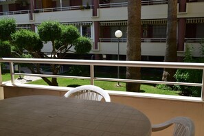 Ein Balkon mit Tisch und Stühlen, der auf einen Innenhof mit Bäumen und einem Gebäude im Hintergrund blickt.