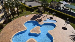 Una piscina dal design particolare, circondata da una zona pavimentata con palme e un piccolo edificio.