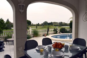 A dining area with a view of a swimming pool and garden.