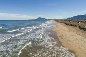 Una playa con olas, una persona caminando y montañas al fondo.