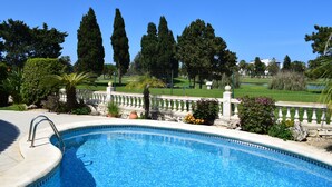 A swimming pool with a stone edge, surrounded by a white balustrade, with a view of a golf course and tall trees in the background. - Ch1100 in Oliva With 2 Bedrooms and 2 Bathrooms (Oliva)