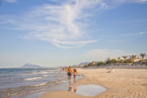 A beach with people walking along the shore, a clear sky, and a distant mountain.