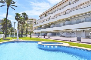 A hotel with a swimming pool, palm trees, and a multi-story building with balconies. - Ap3208 in Denia With 3 Bedrooms and 2 Bathrooms (Denia)
