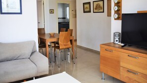 Egy modern nappali, melyben kanapé, étkezőasztal, székek és egy televízió található, a televízió egy fa szekrényen van elhelyezve.