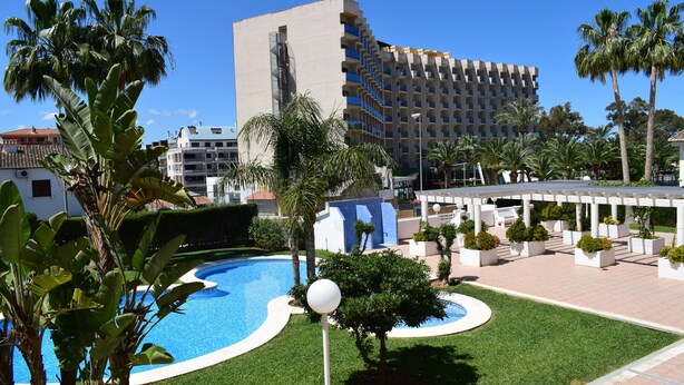 Un hôtel doté d’une piscine, de palmiers et d’un bâtiment moderne avec des balcons.
