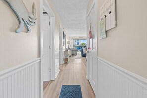 A hallway with white wainscoting, a blue rug, and a view of a pool and outdoor seating area. - Oceanview Shore Dr  2BR Condo (Myrtle Beach)