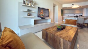 A modern living room with a wooden coffee table, a TV on a white stand, and a kitchen in the background. - 37th Floor OCEAN VIEW Retreat - 2BR Hollywood (Hollywood)