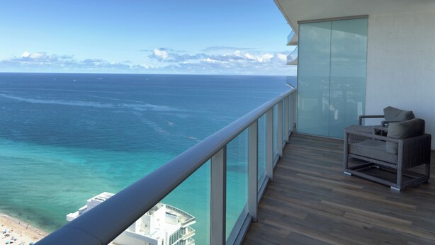 A balcony with a view of the ocean and beach, wooden flooring, and a wicker chair. - 37th Floor OCEAN VIEW Retreat - 2BR Hollywood (Hollywood)