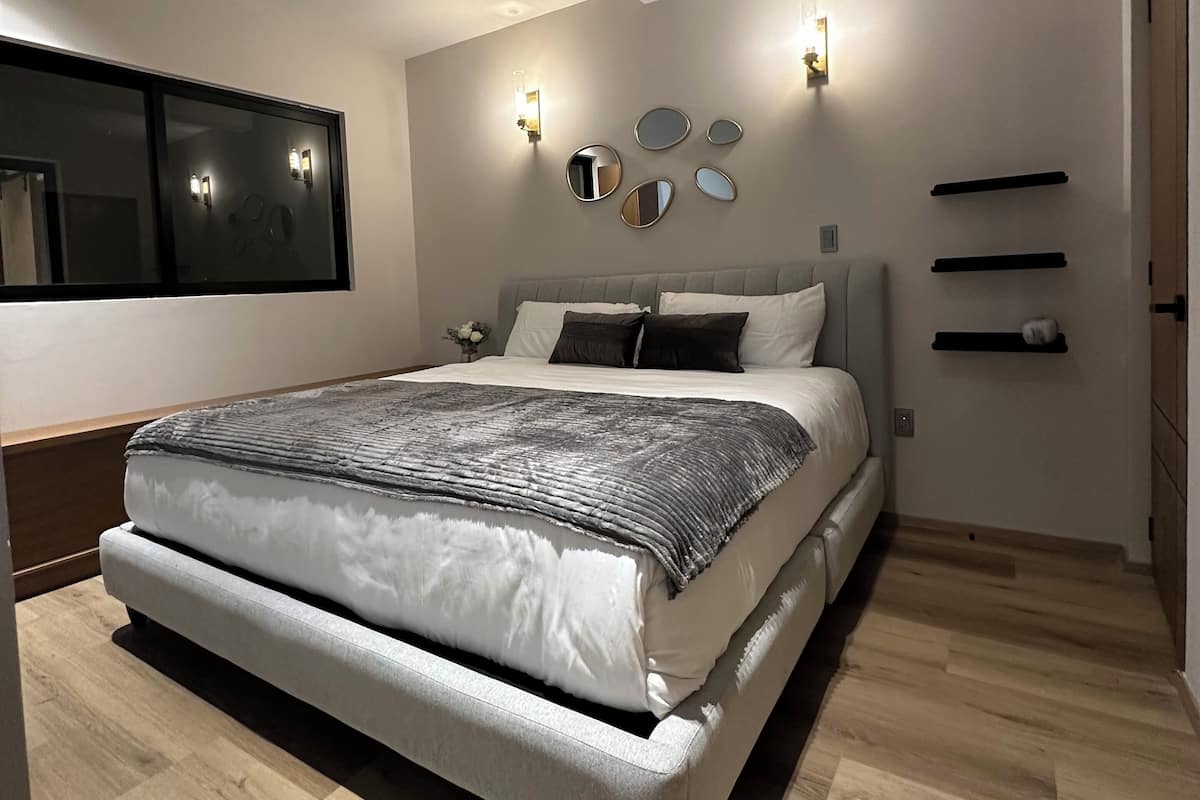 A modern bedroom with a large bed, a wall-mounted mirror, and a bedside shelf.