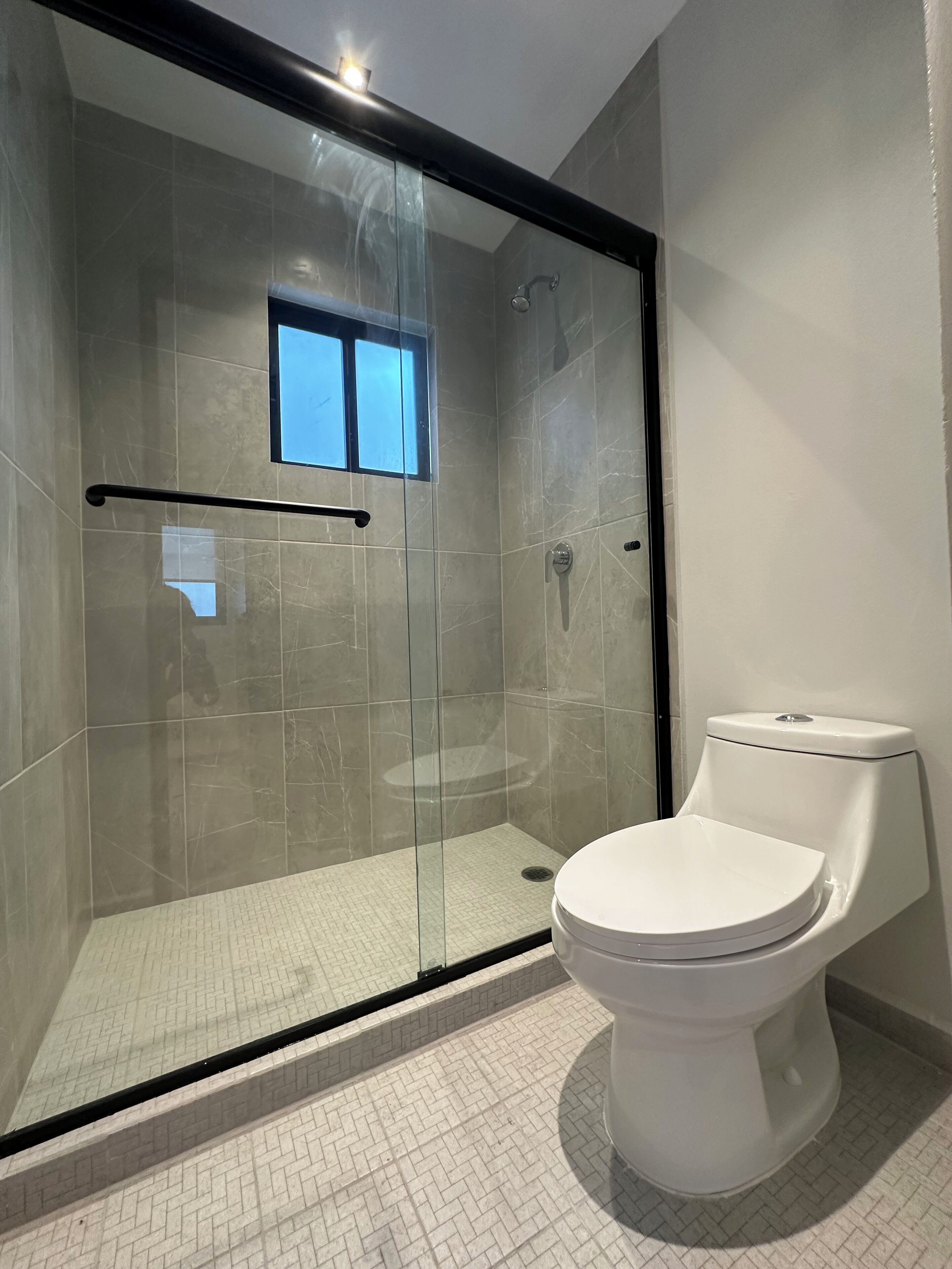 Une salle de bain moderne avec une douche à parois de verre, des toilettes blanches et une petite fenêtre.