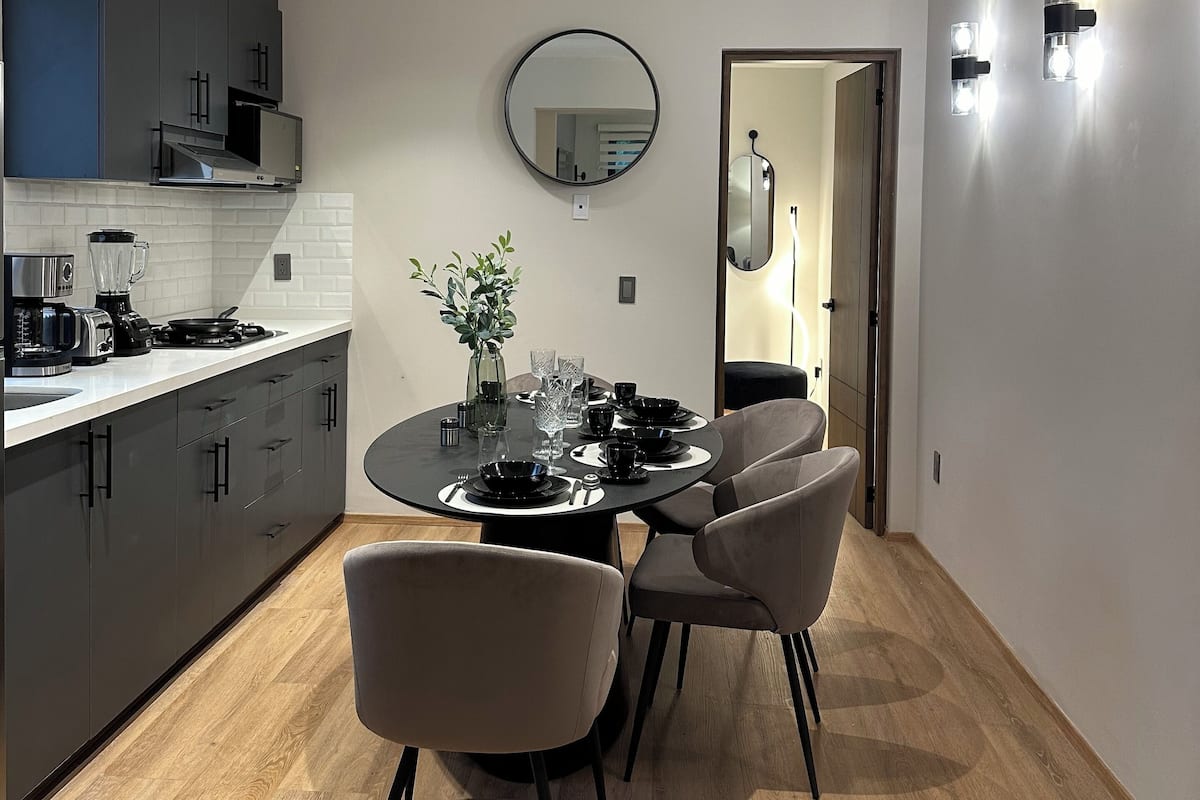 A modern kitchen with dark cabinets, a round mirror, and a dining area with a table set for four.
