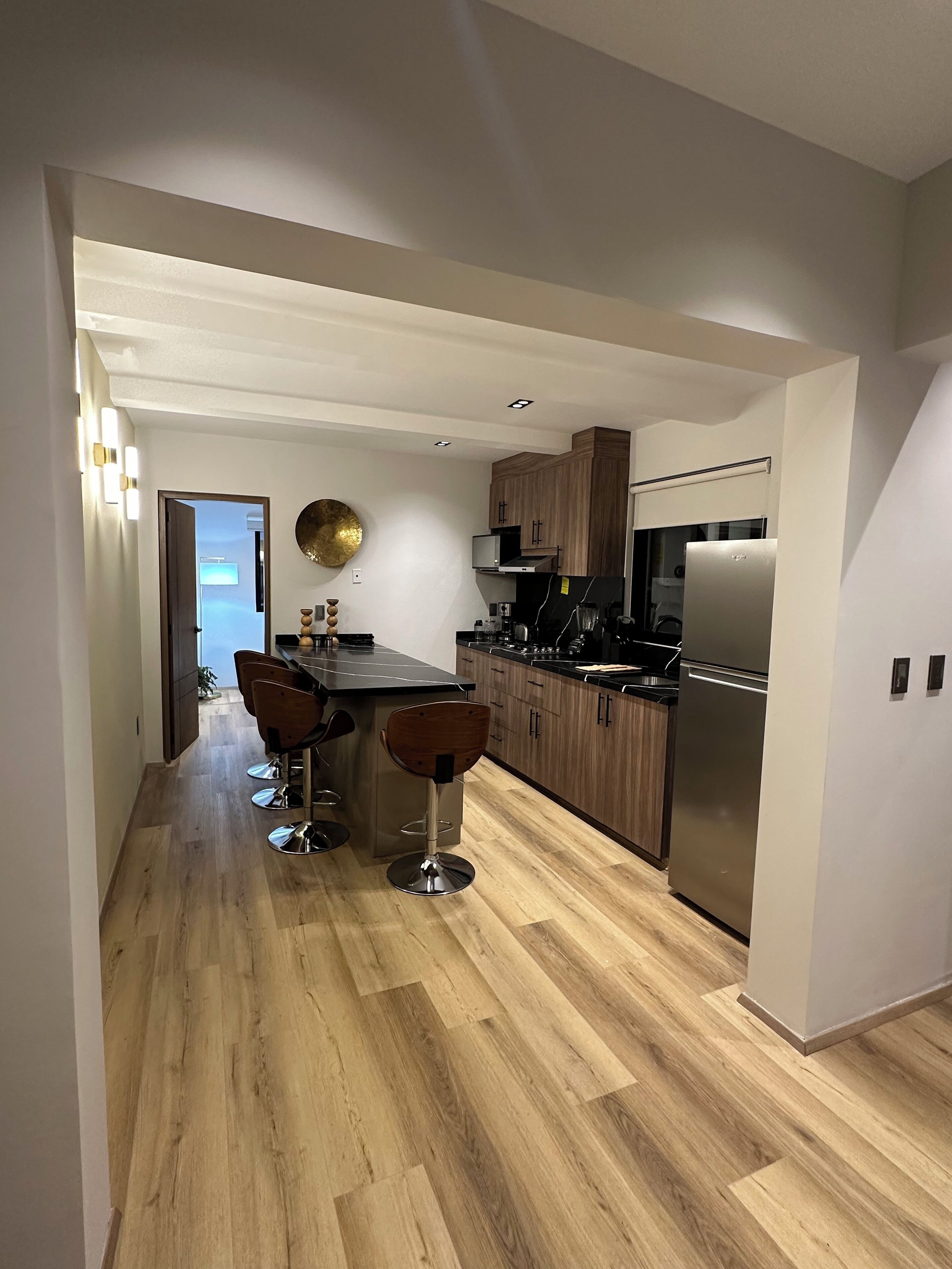 A modern kitchen with wooden cabinets, a stainless steel refrigerator, and a bar area with stools.