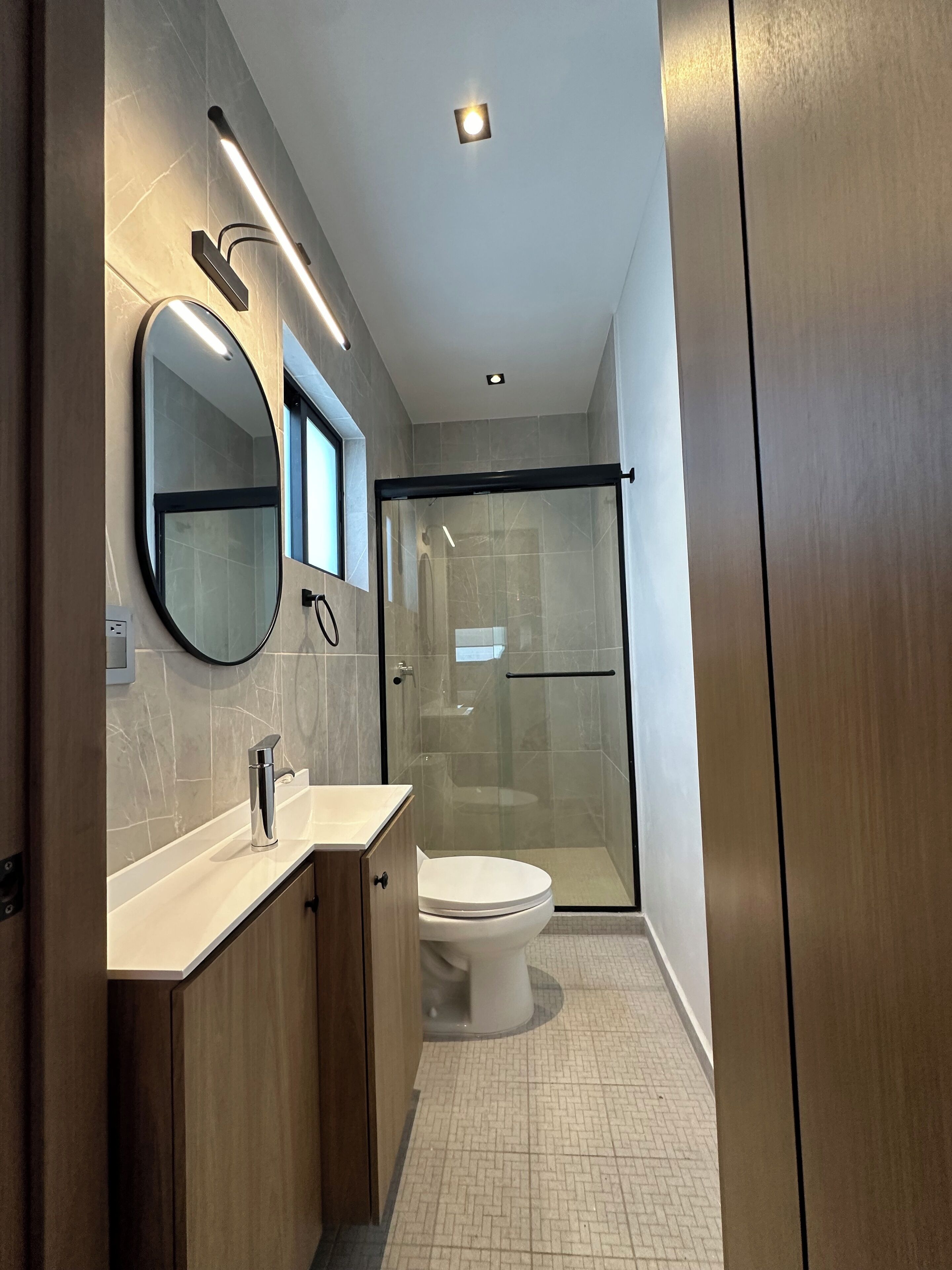 A modern bathroom with a glass-enclosed shower, a round mirror, and a white toilet.