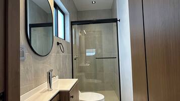 A modern bathroom with a glass-enclosed shower, a round mirror, and a white toilet.