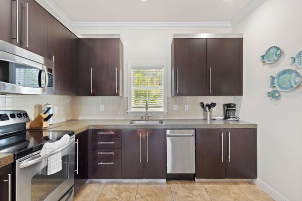 A modern kitchen with dark cabinets, stainless steel appliances, and a window with blinds. - The Beach Club at Siesta Key- 101E Condo (Sarasota)