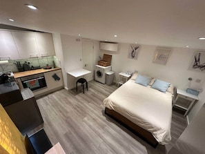A modern bedroom with a large bed, a desk, a washing machine, and a small kitchen area. - Cosy, self-contained guest house (London)