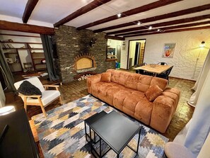 A cozy living room with a stone fireplace, a sofa, a dining table, and a patterned rug. - CASA-Blizzard 2 chambres apt à Saint-Véran (Molines-en-Queyras)