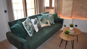A green sofa with patterned cushions, a round wooden coffee table with a plant, and a brick wall. - Apartment & Boutique Meraki 1 bedroom. (Ontinyent)