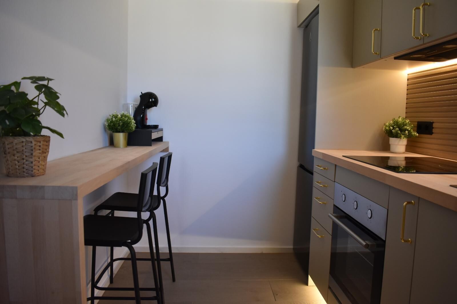 Una cocina compacta con encimera de madera, dos sillas negras, horno empotrado y una pequeña planta en maceta.